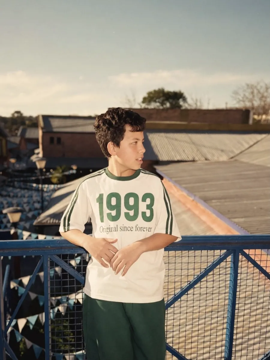 Chico en una terraza con remera crema y verde 1993 y pantalón verde